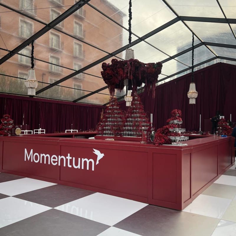 A large red counter with the word "Momentum" prominently displayed, surrounded by a lavish and ornate decor, including a chandelier and a checkered floor, in what appears to be an indoor event space or lobby.