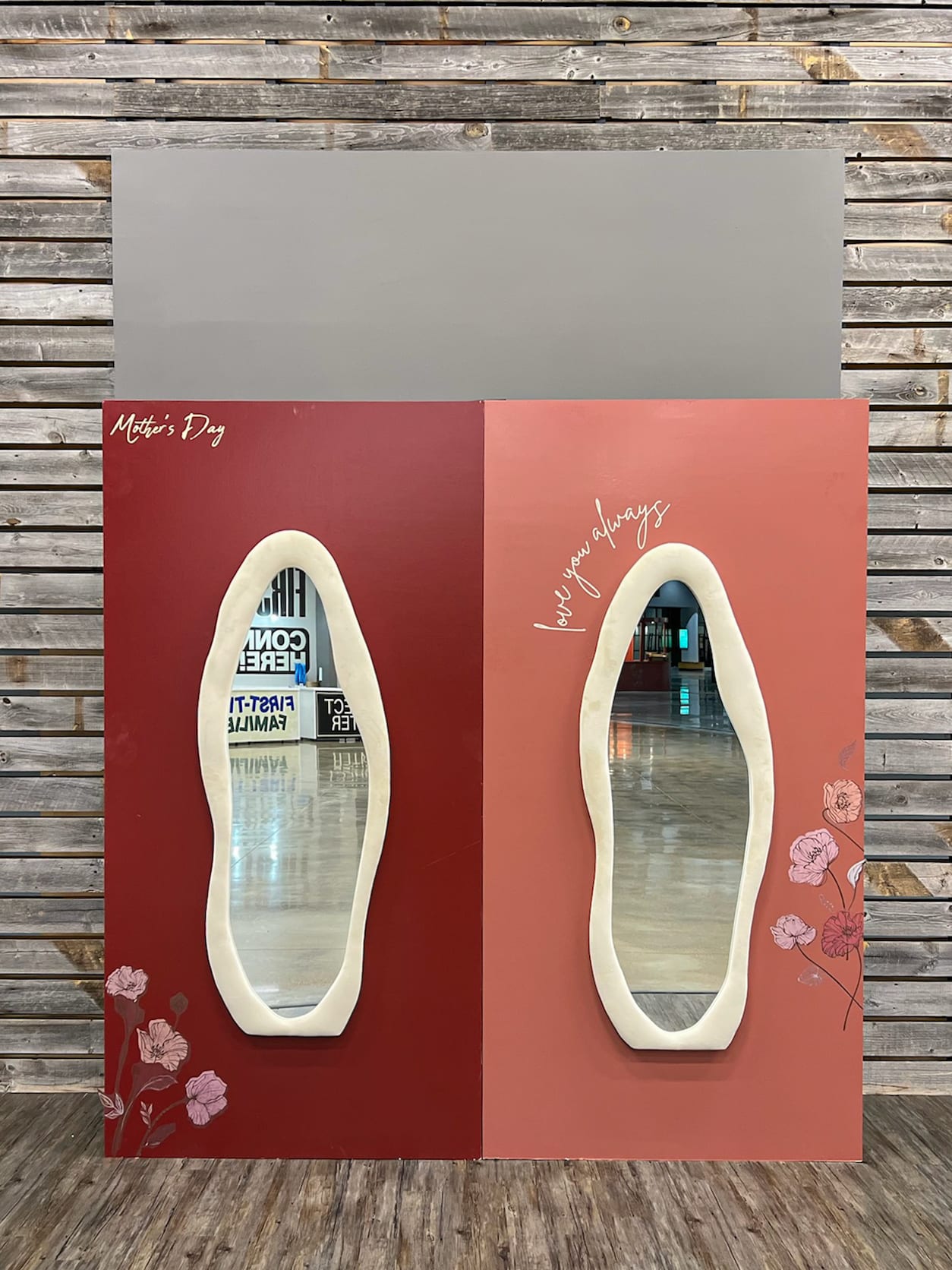 The image shows two oval-shaped mirrors mounted on a red background, with a wooden wall in the background.