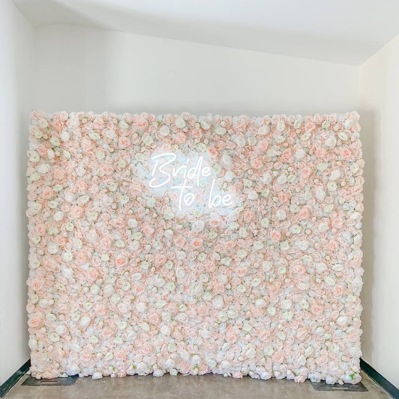 a white wall with pink flowers and a white sign that says bride to be on the side of it