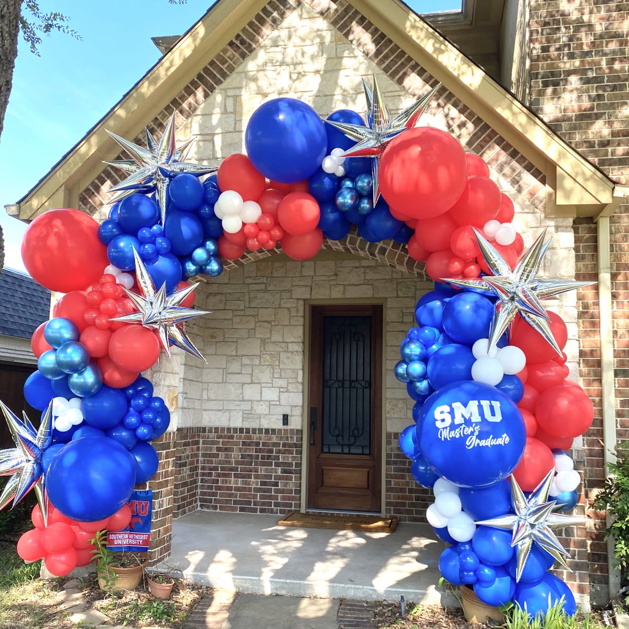 a red, white and blue balloon arch in front of a house with a flag and stars on it