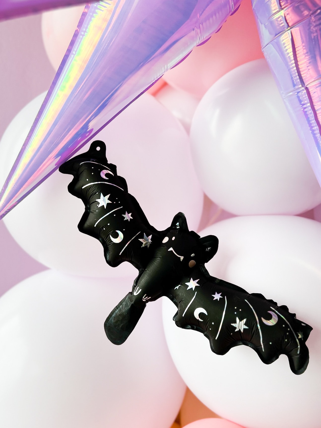 A black bat-shaped hair clip or accessory is prominently displayed against a vibrant, pastel-colored background with a soft, blurred effect.
