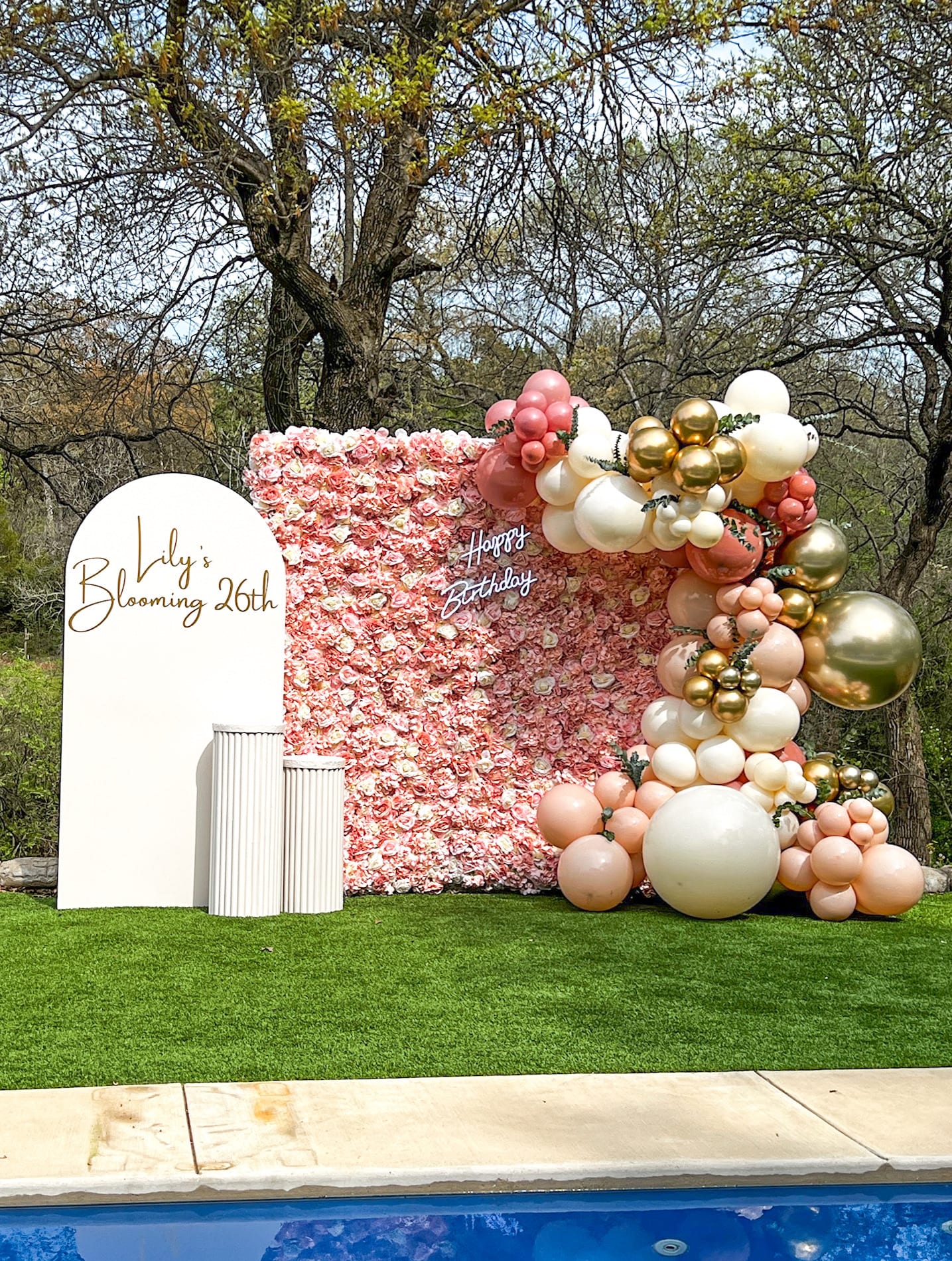 A vibrant and whimsical balloon display adorns a grassy outdoor setting, with a large white sign in the foreground celebrating a 26th birthday.