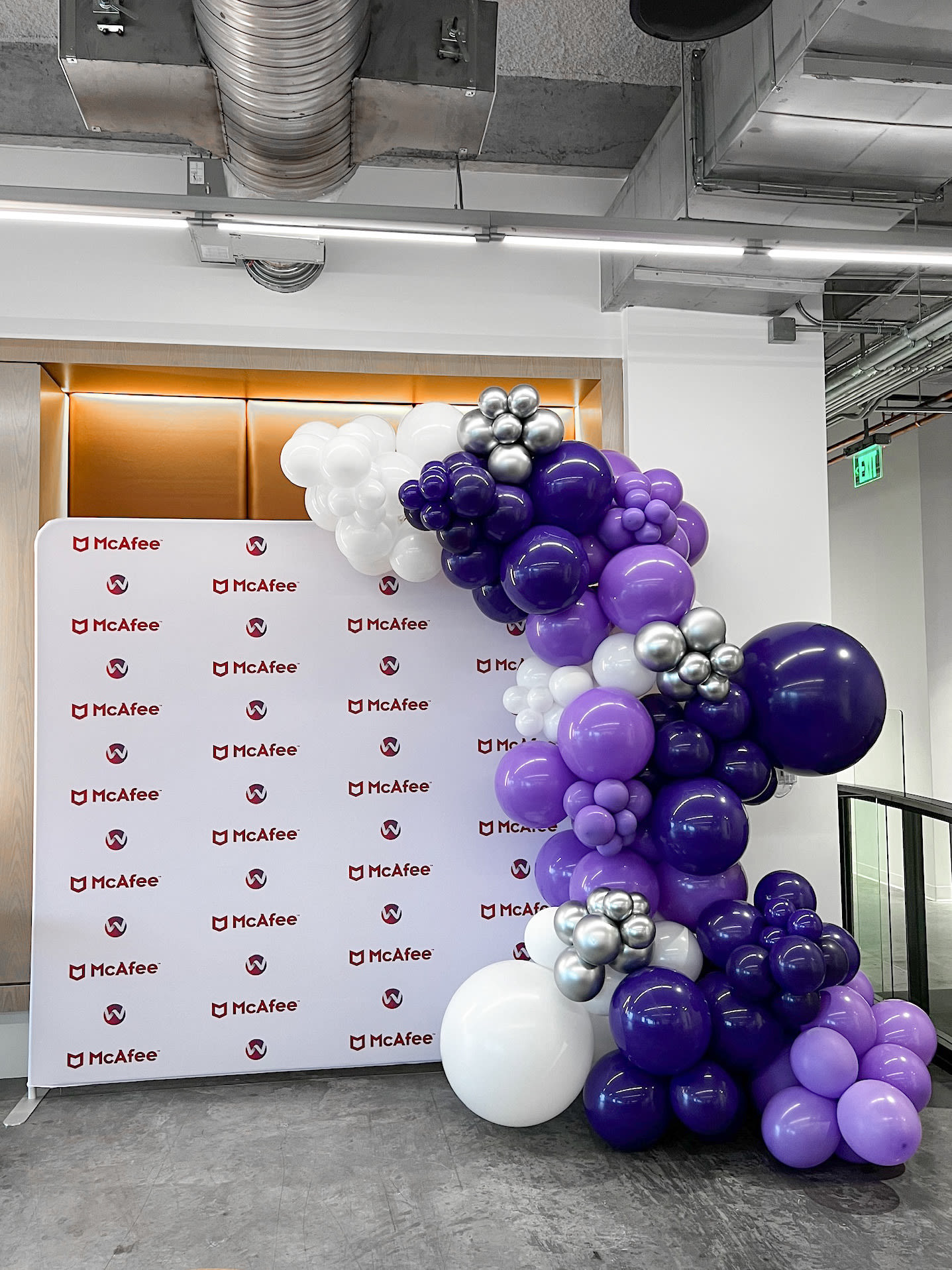 A large display of colorful balloons, primarily in shades of purple and white, is set against a backdrop of branded signage and a gray industrial-style ceiling.