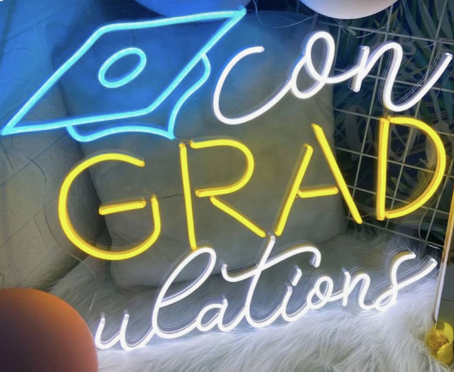 a neon sign that reads zoom grad questions on a white furnishing next to balloons and a stuffed animal
