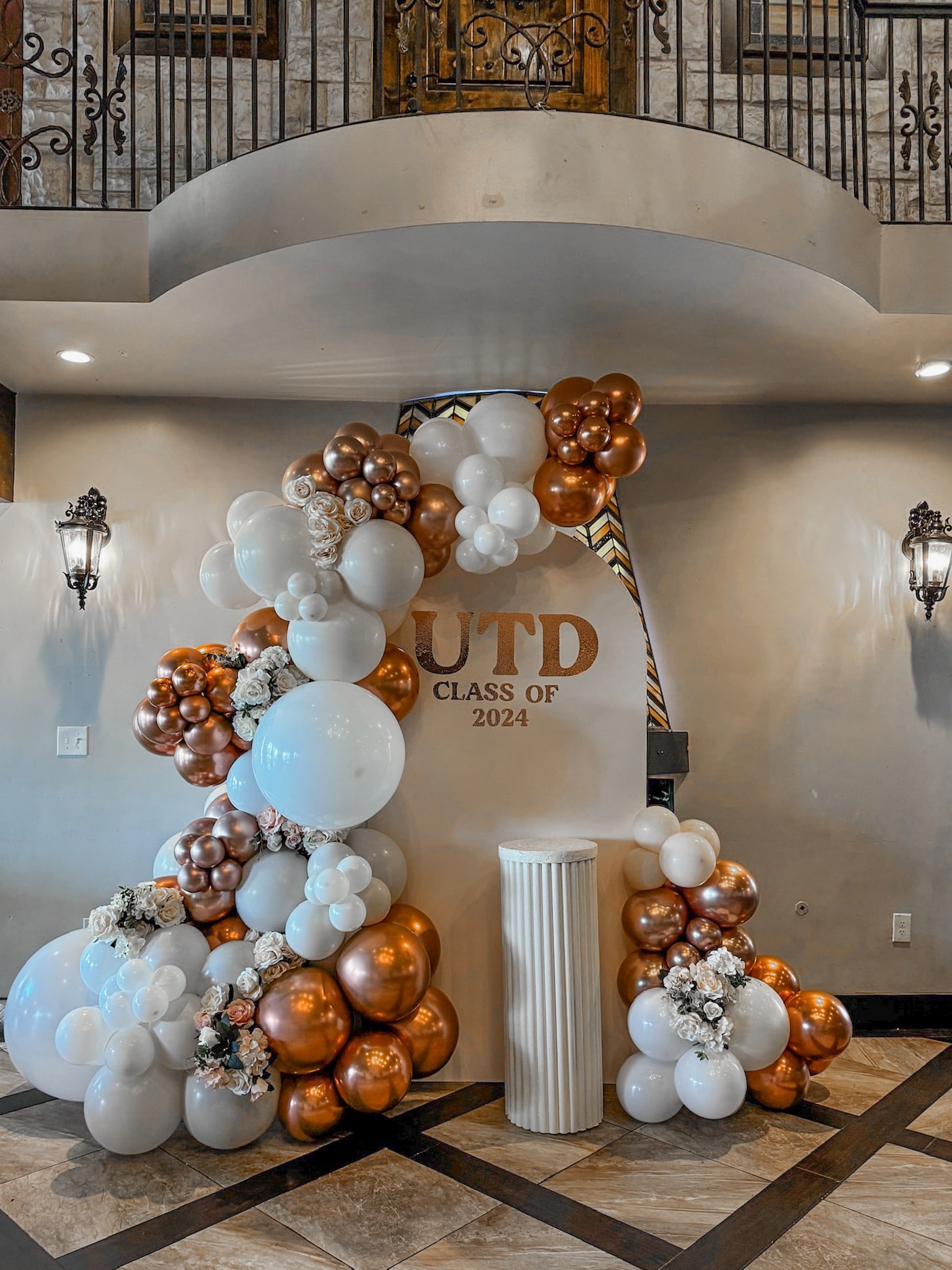 A decorative balloon arch in shades of white, gold, and bronze adorns the entrance, with the text "GRD Class of 2024" prominently displayed, set against a backdrop of ornate architectural features.