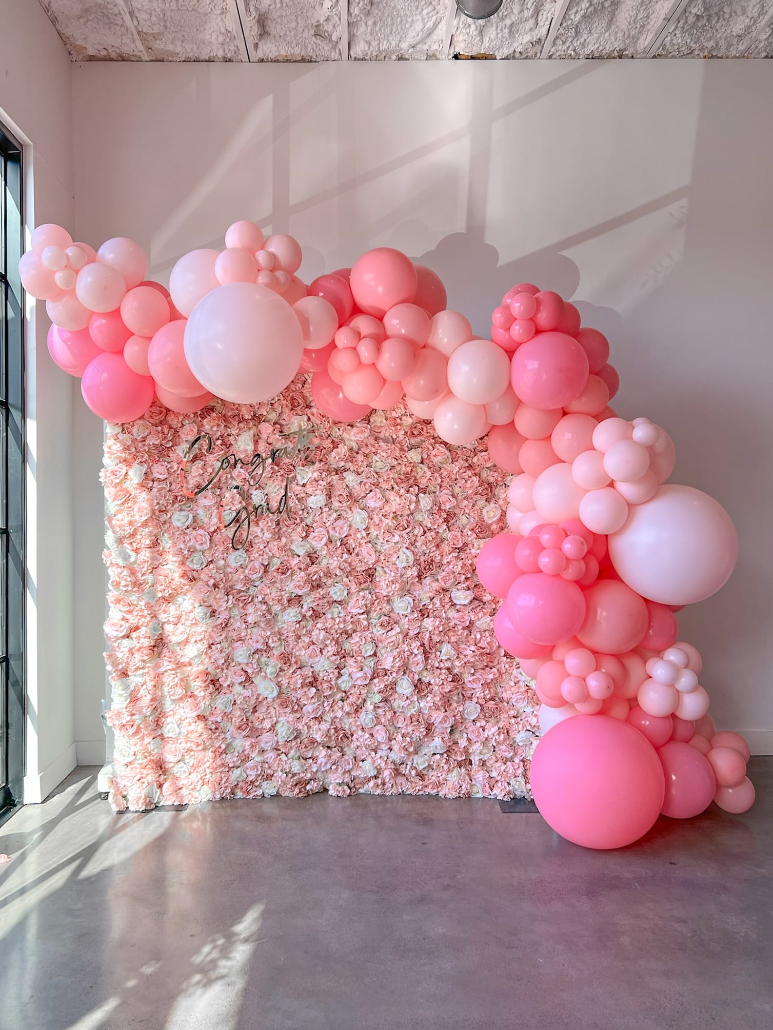 A vibrant display of pink and white balloons arranged in an artistic, organic manner, creating a visually striking backdrop against a plain wall.