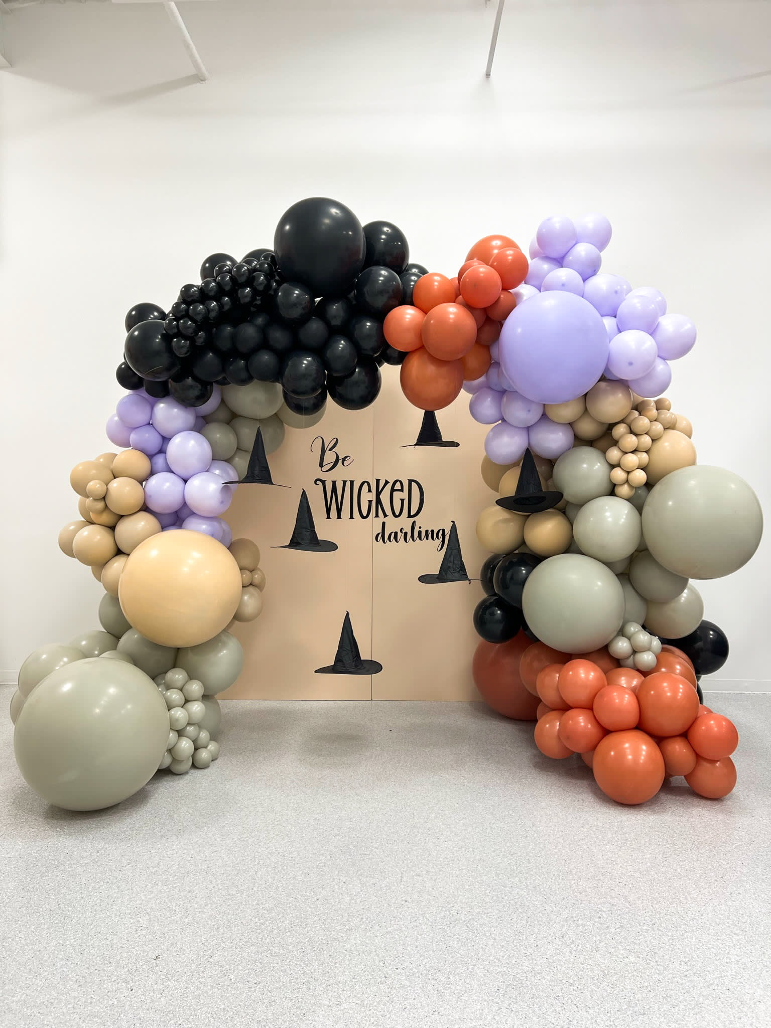 A vibrant and whimsical display of various colorful balloons, fruits, and other decorative elements arranged in a visually striking manner, with the text "A Wicked Gathering" prominently featured.
