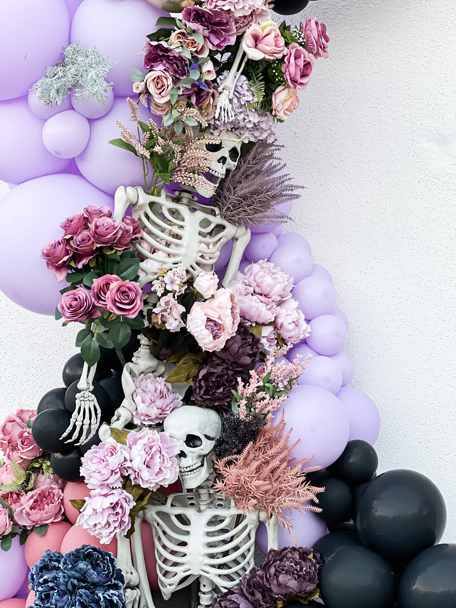 A striking arrangement of skeletal figures, vibrant flowers, and soft purple balloons creates a captivating and visually striking composition.