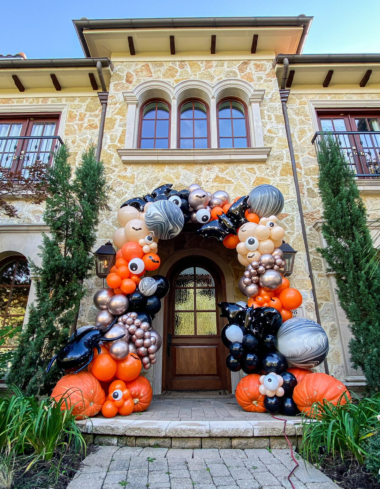 A grand, stone-clad building with arched windows and a decorative entryway is adorned with a vibrant display of colorful balloons and pumpkins, creating a festive and welcoming atmosphere.