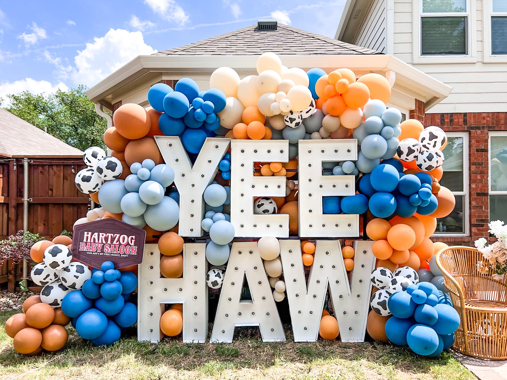 A large, colorful display of balloons and letters spelling out "YEE HAW" is set against the backdrop of a residential house with a tiled roof and windows.