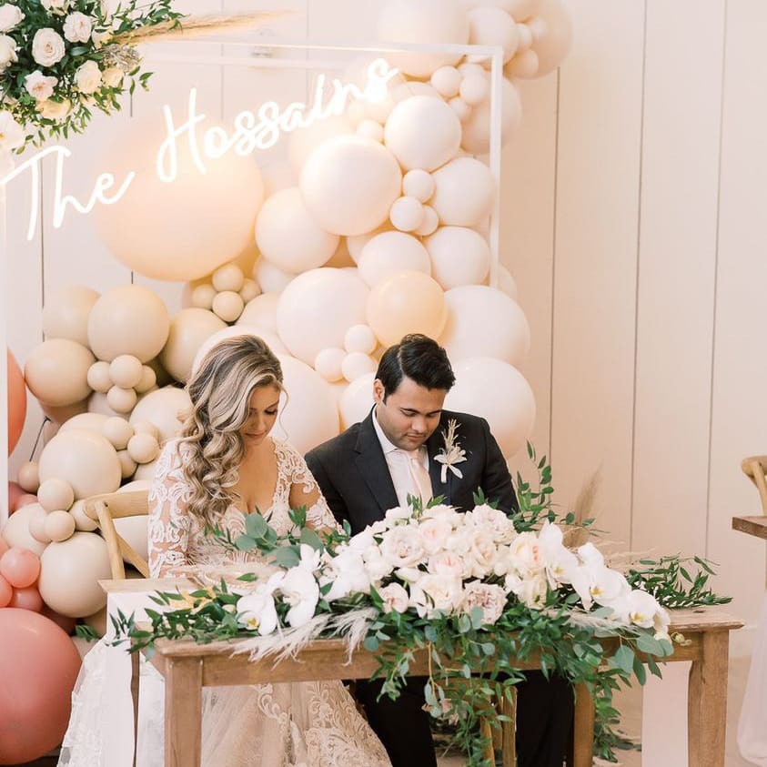 a man and a woman sitting at a table with a bouquet of flowers and balloons in front of them