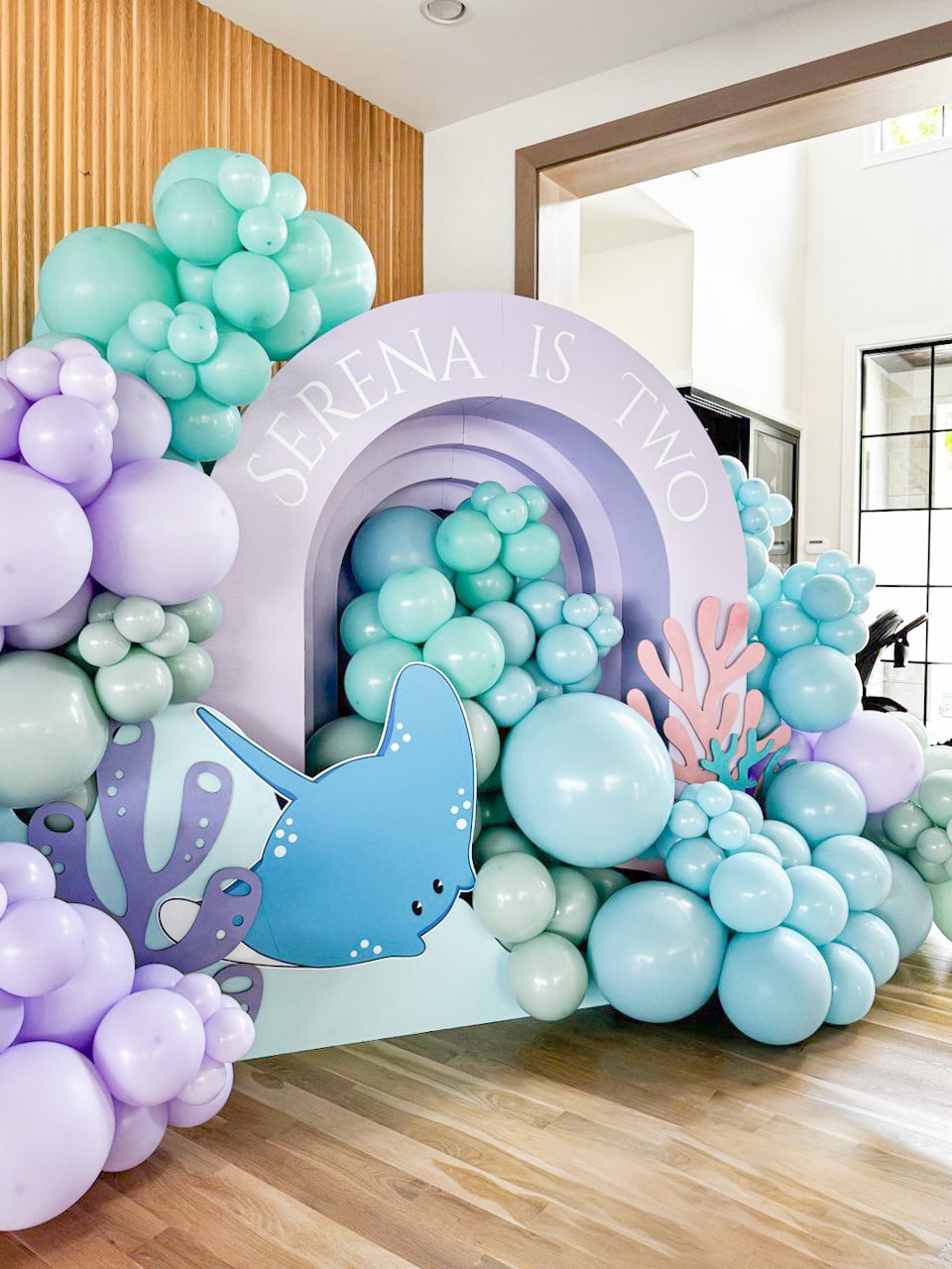The image features a colorful and whimsical underwater-themed display, with a large rainbow arch, various pastel-colored balloons and shapes resembling coral and sea creatures, creating a vibrant and imaginative scene.