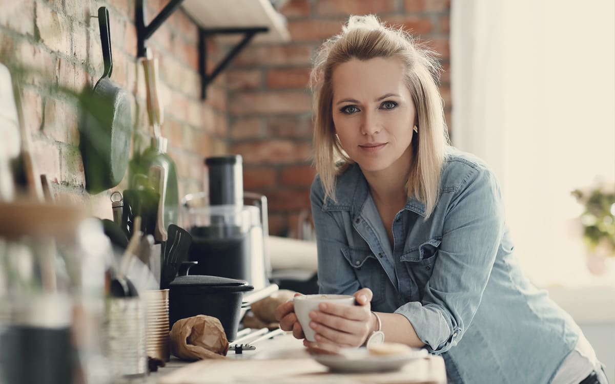 Frau mit Kaffeetasse in der Küche.
