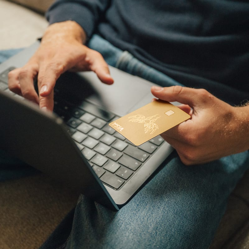 Person hält eine goldene Bank Norwegian Visa-Karte in der Hand und bezahlt online am Laptop