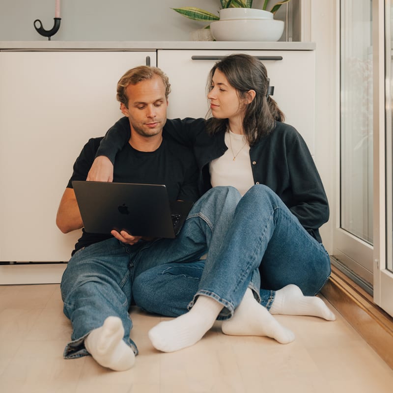 Ett par sitter på köksgolvet och tittar tillsammans på en laptop