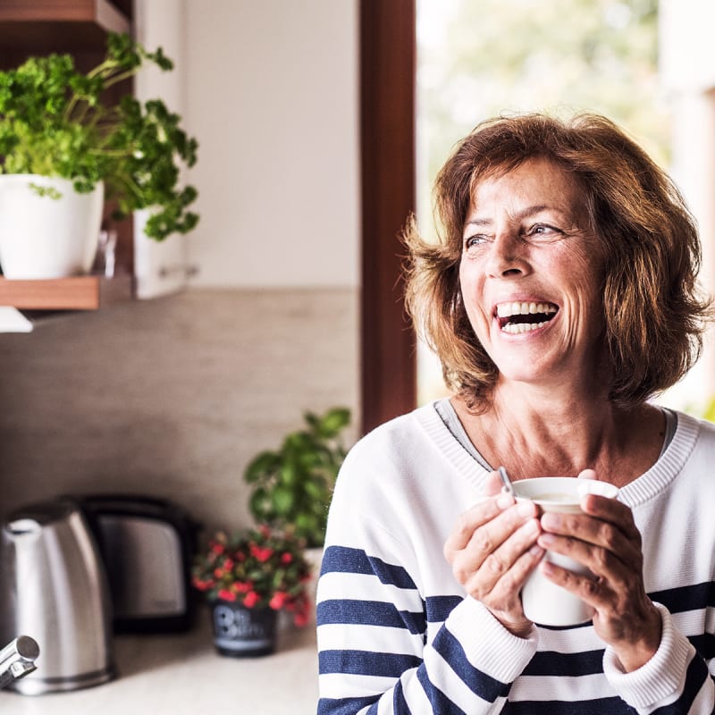 Happy elderly woman drinking a cup of coffee in her kitchen