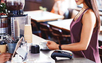 Dame som betaler med en Fitbit-klokke på en kontaktløs betalingsterminal med ditt Bank Norwegian kredittkort