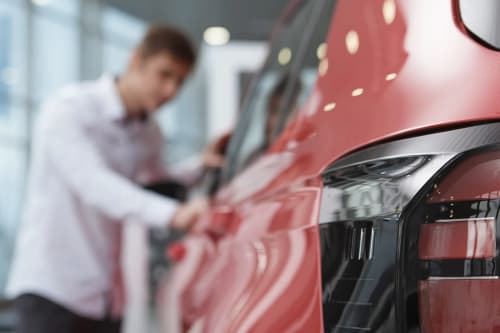 Nærbilde av baklykten på en rød bil i en bilbutikk, med en mann som ser på bilen i bakgrunnen.