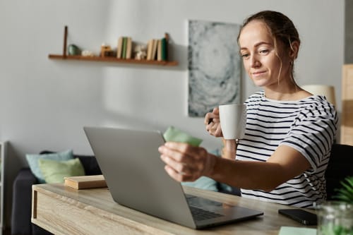 Kvinne foran laptop med en kaffekopp i hånden