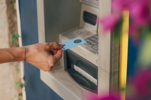 Hånd som setter inn et Bank Norwegian-kort i en minibank for å ta ut kontanter