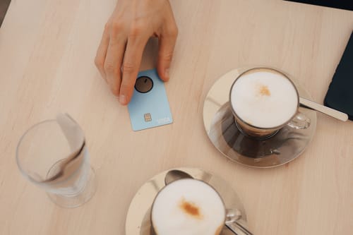 Hånd holder Bank Norwegian-kortet på et kafébord med to kaffekopper
