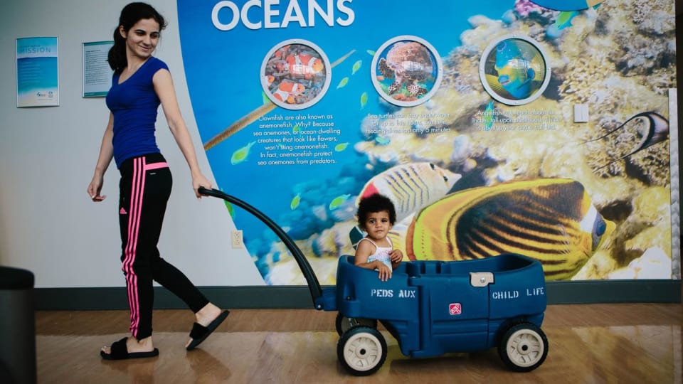 a woman pulls her toddler through a hallway at Wolfson in a plastic blue wagon