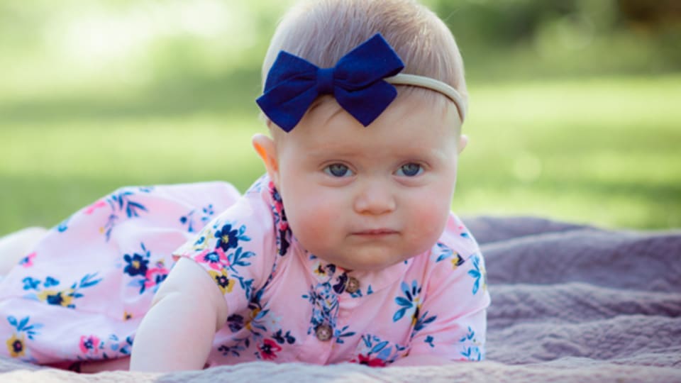 baby girl with a blue bow in her hair laying on a blanket outside in the middle of a park