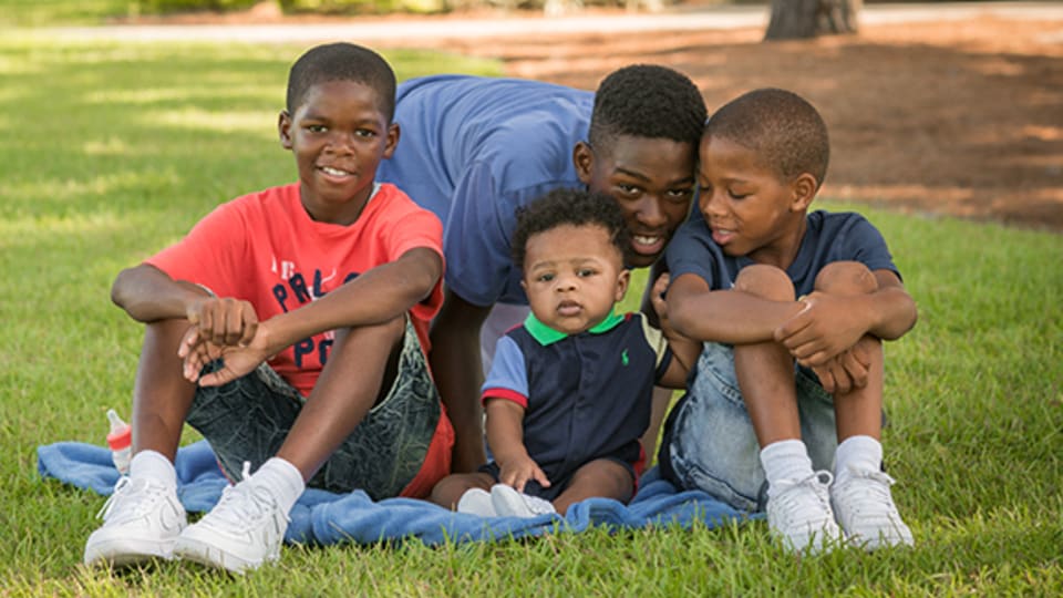 4 smiling brothers sitting together on a blanket in the middle of a park