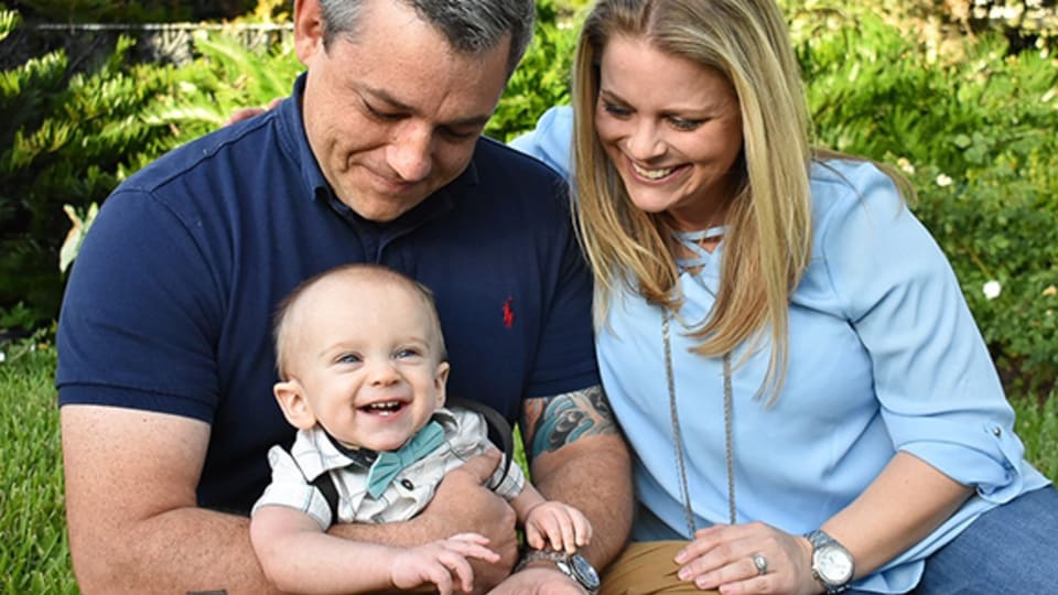 smiling couple sits with their baby on the grass outside