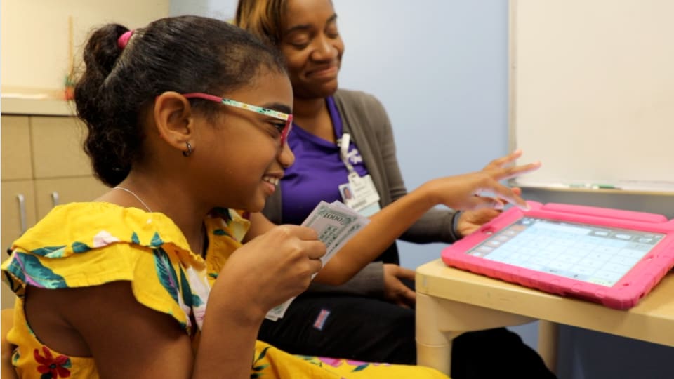 Young girl using a tablet being supervised by a nurse