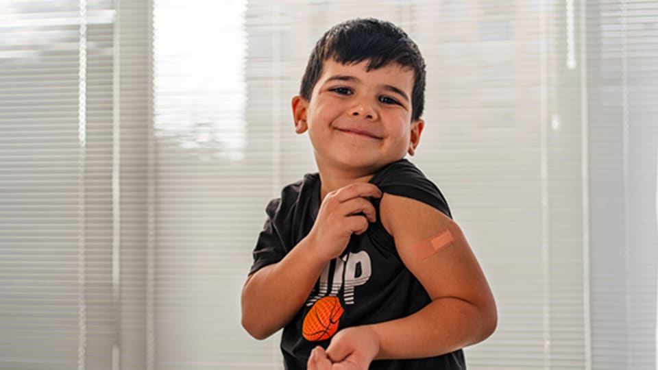 young boy showing his bandaged shoulder after getting a shot