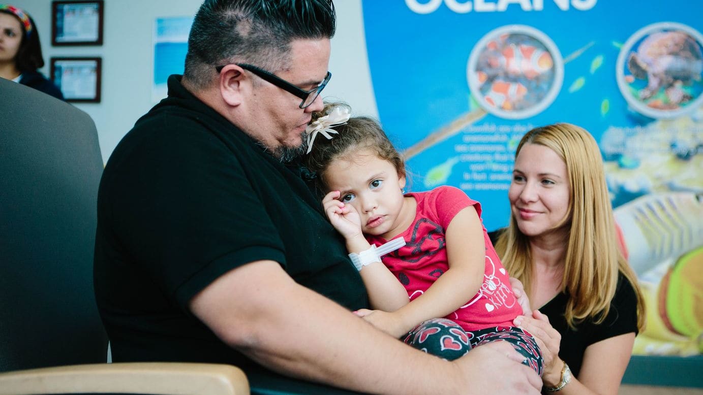 mom and dad comfort their young daughter as they sit in a waiting room at Wolfson Children's Hospital