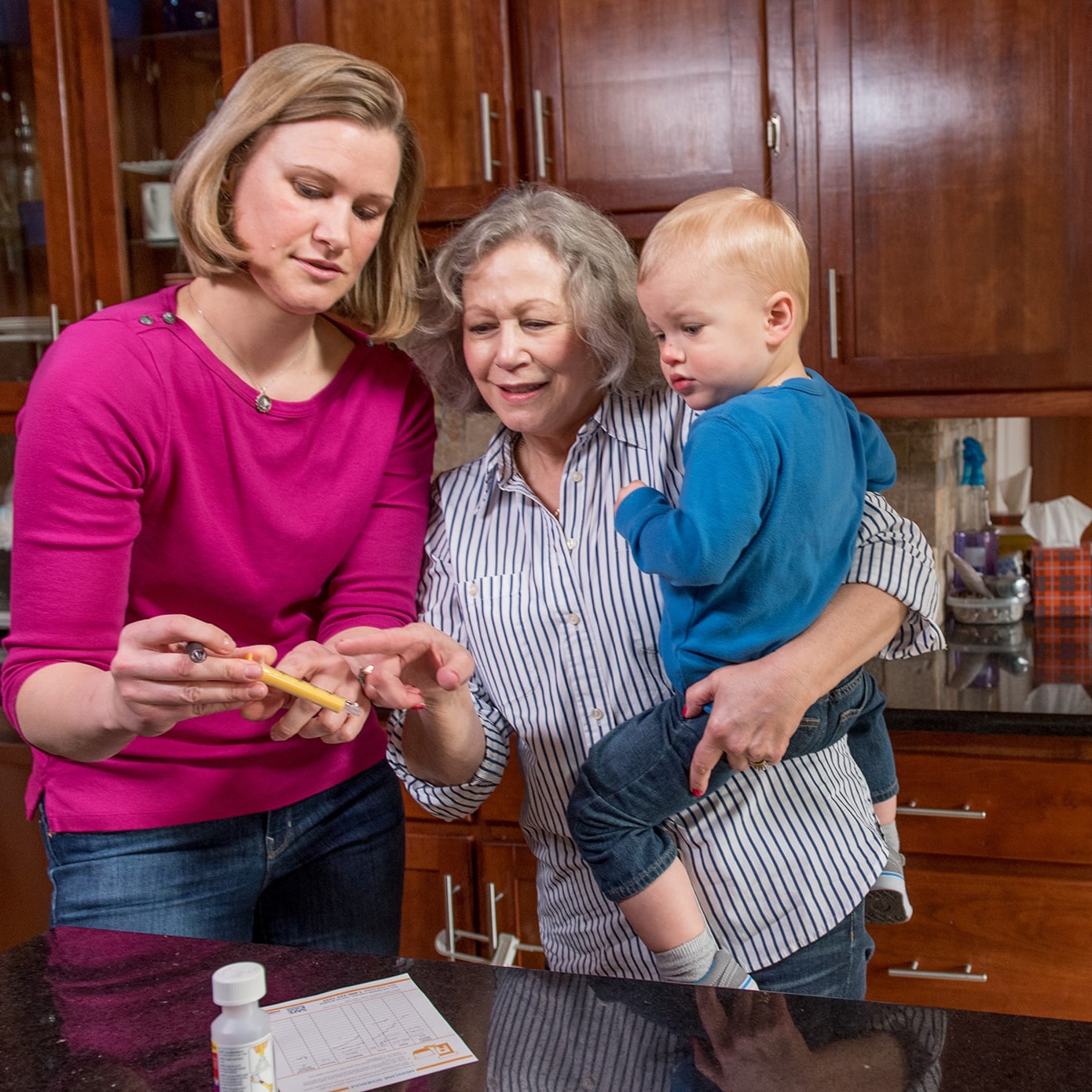 a toddler being held by his grandmother standing next to mom in a home's kitchen.