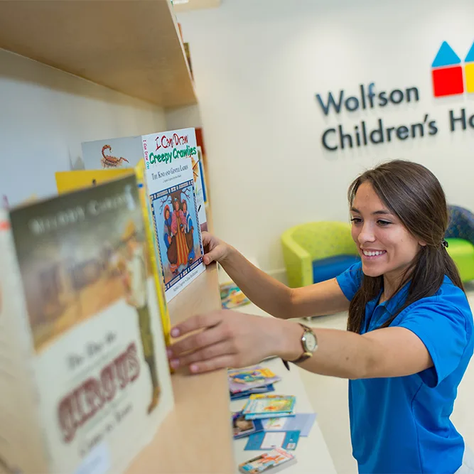 smiling young woman putting books on a bookshelf at Wolfson Children's Hospital
