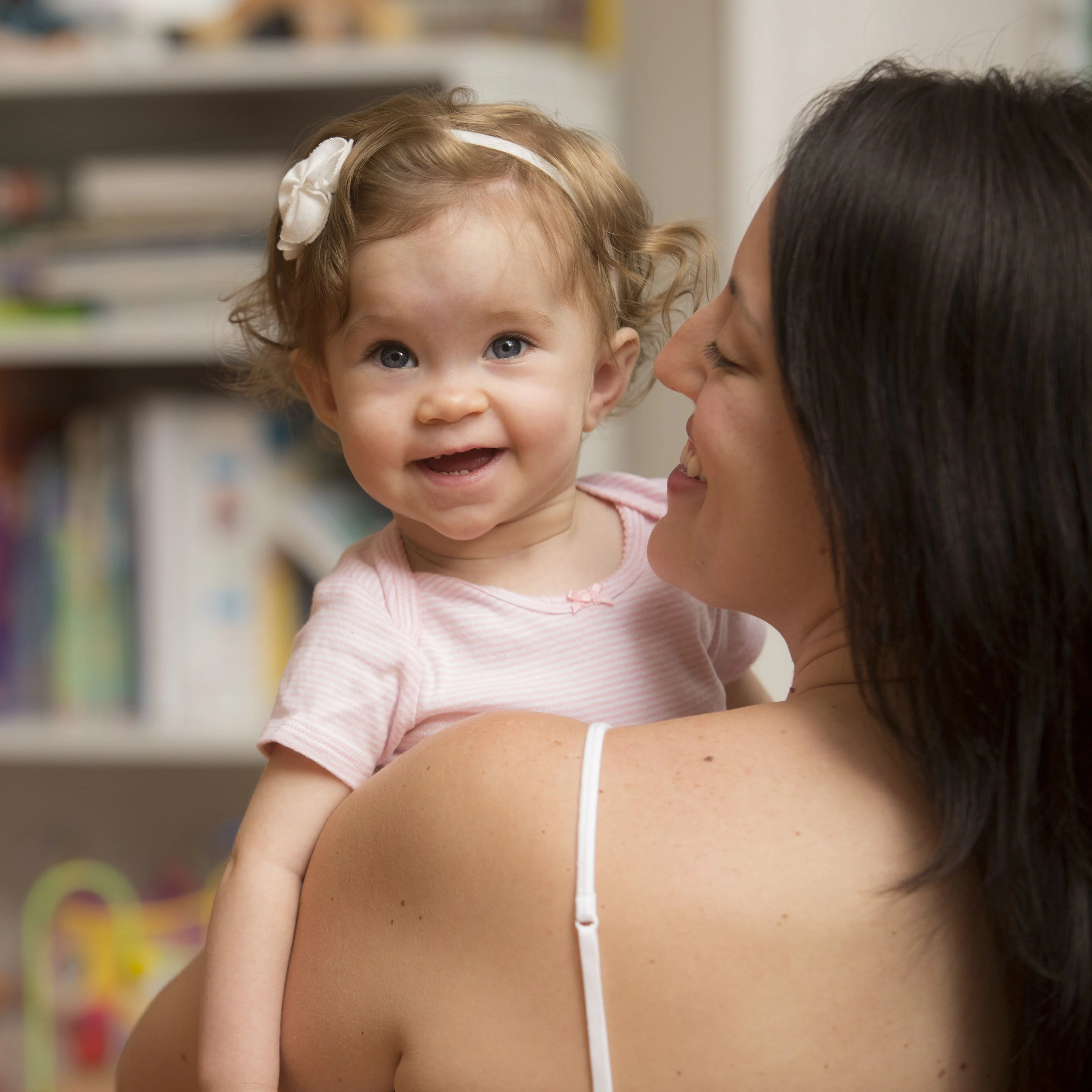 mom and young daughter smile together in front of a bookcase