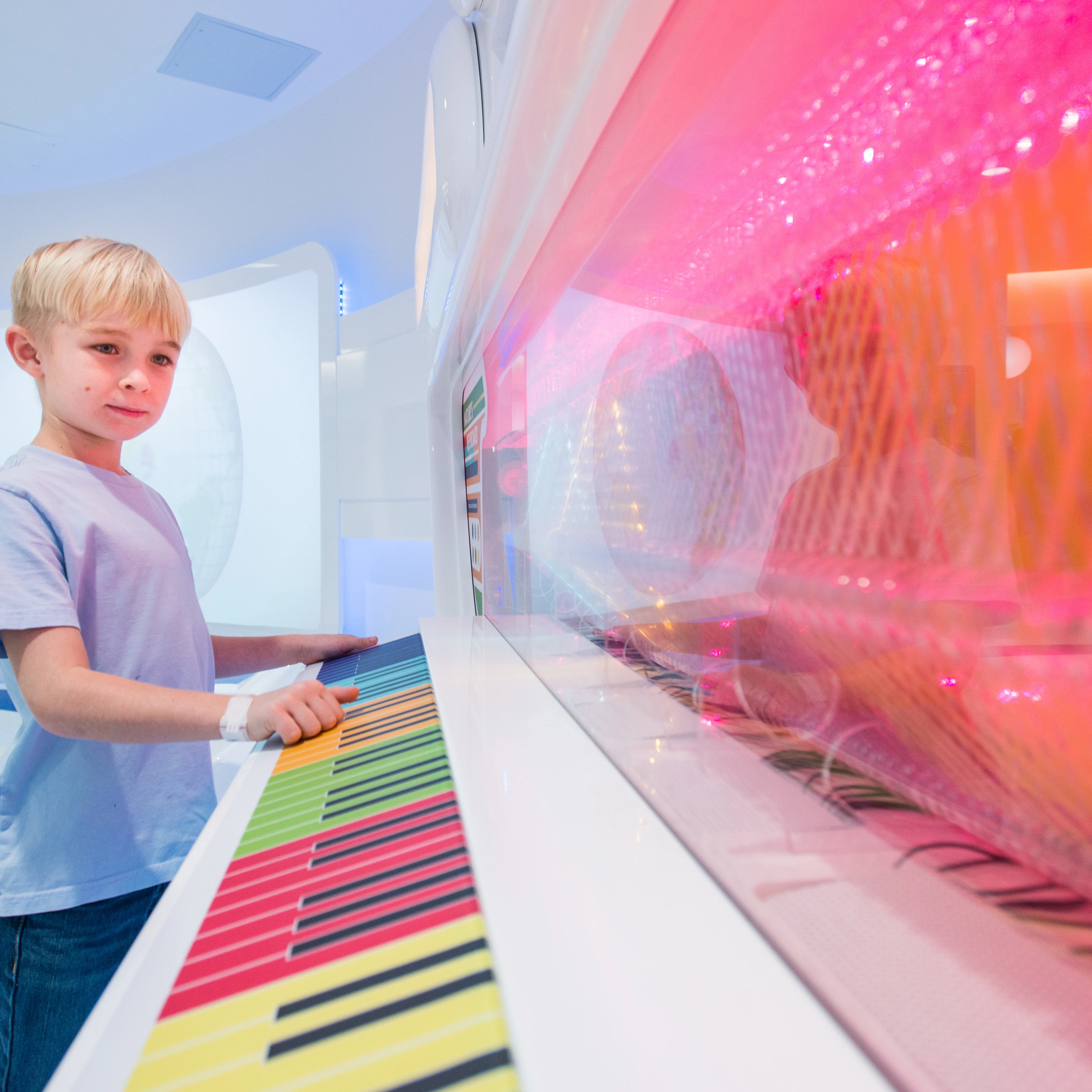 a school-age boy standing in front of a colorful wall of lights