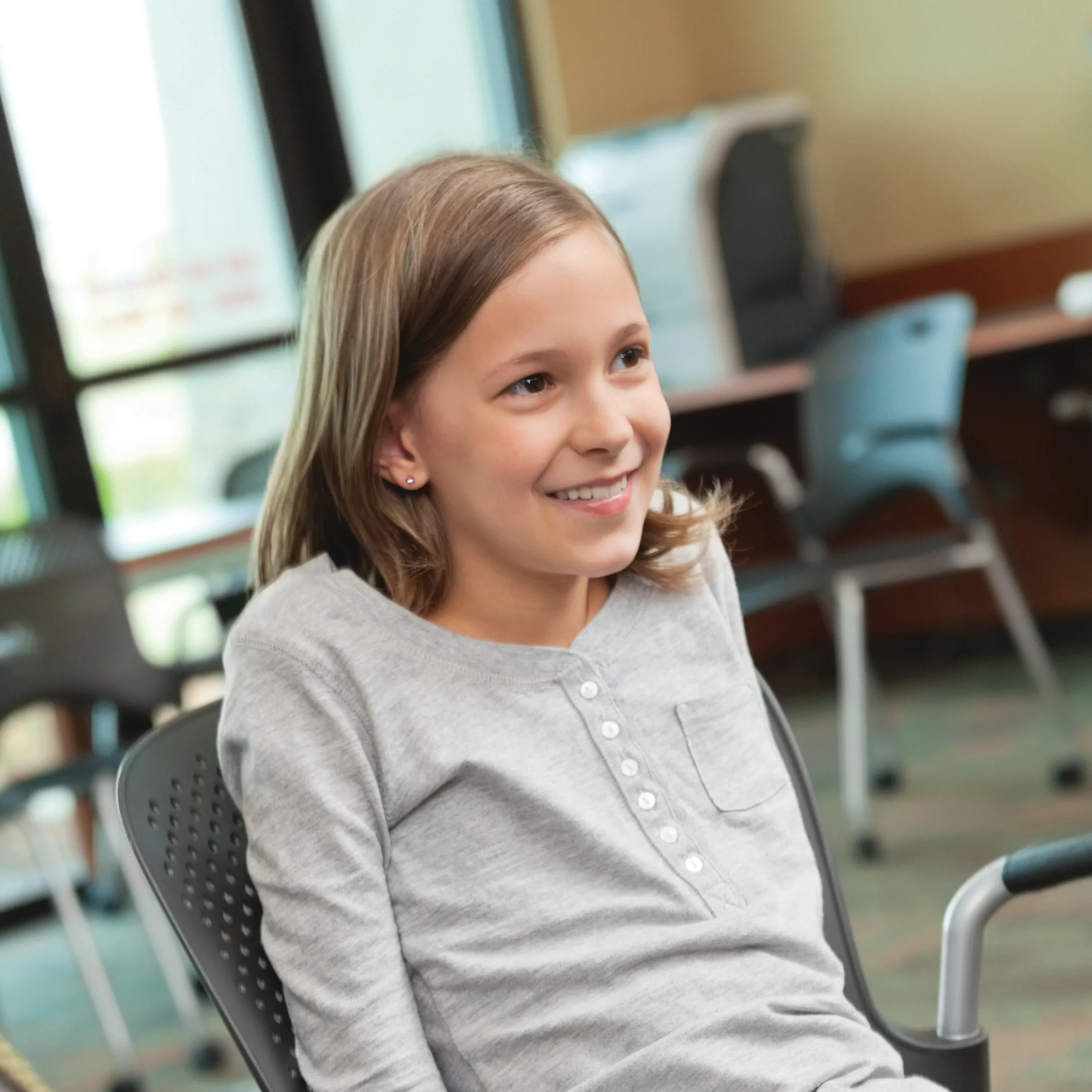 Smiling elementary age girl sitting in a chair in a room with lots of windows