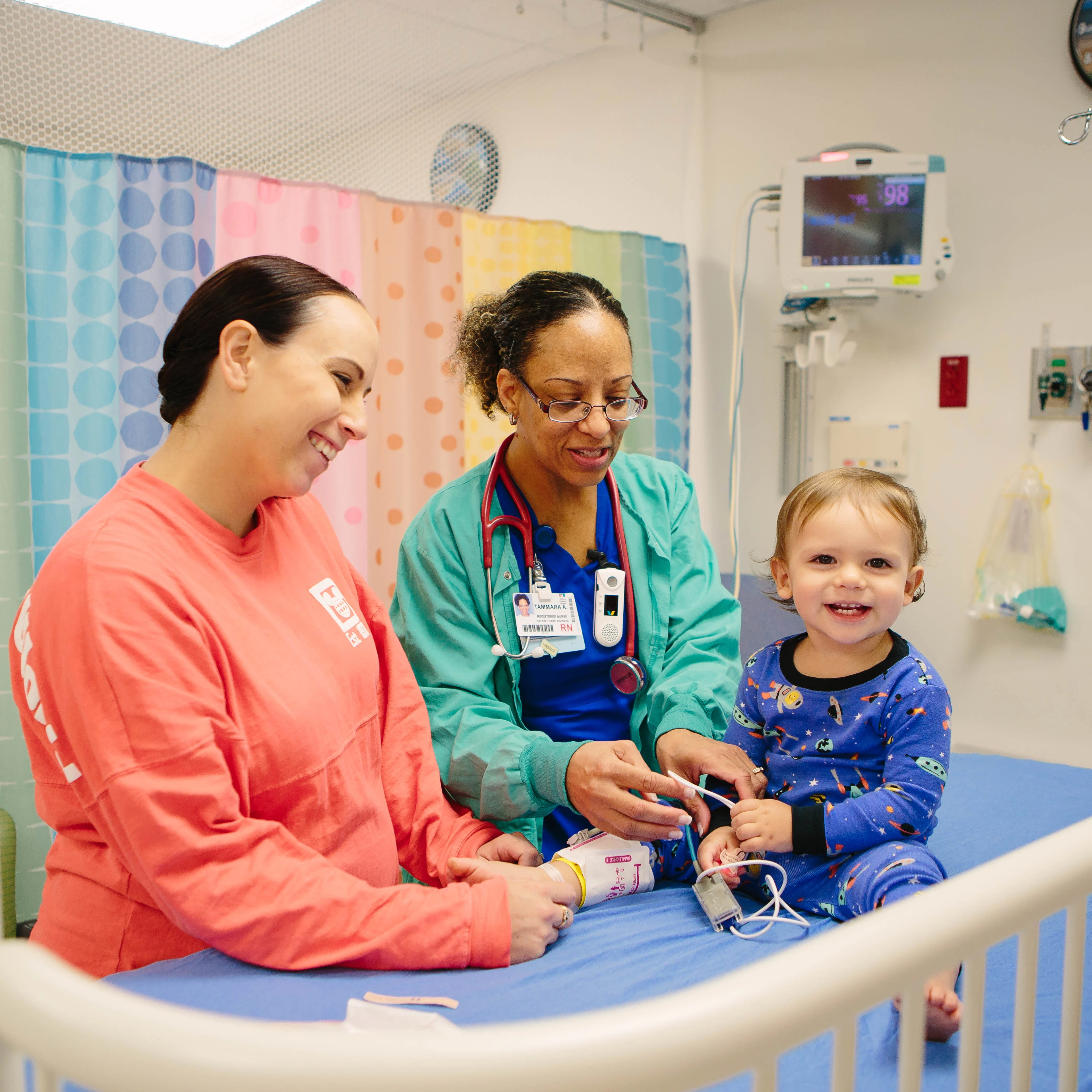 18-month-old boy sitting on a hospital bed smiling with his mom and a female nurse before his ENT treatment, tube-replacement surgery