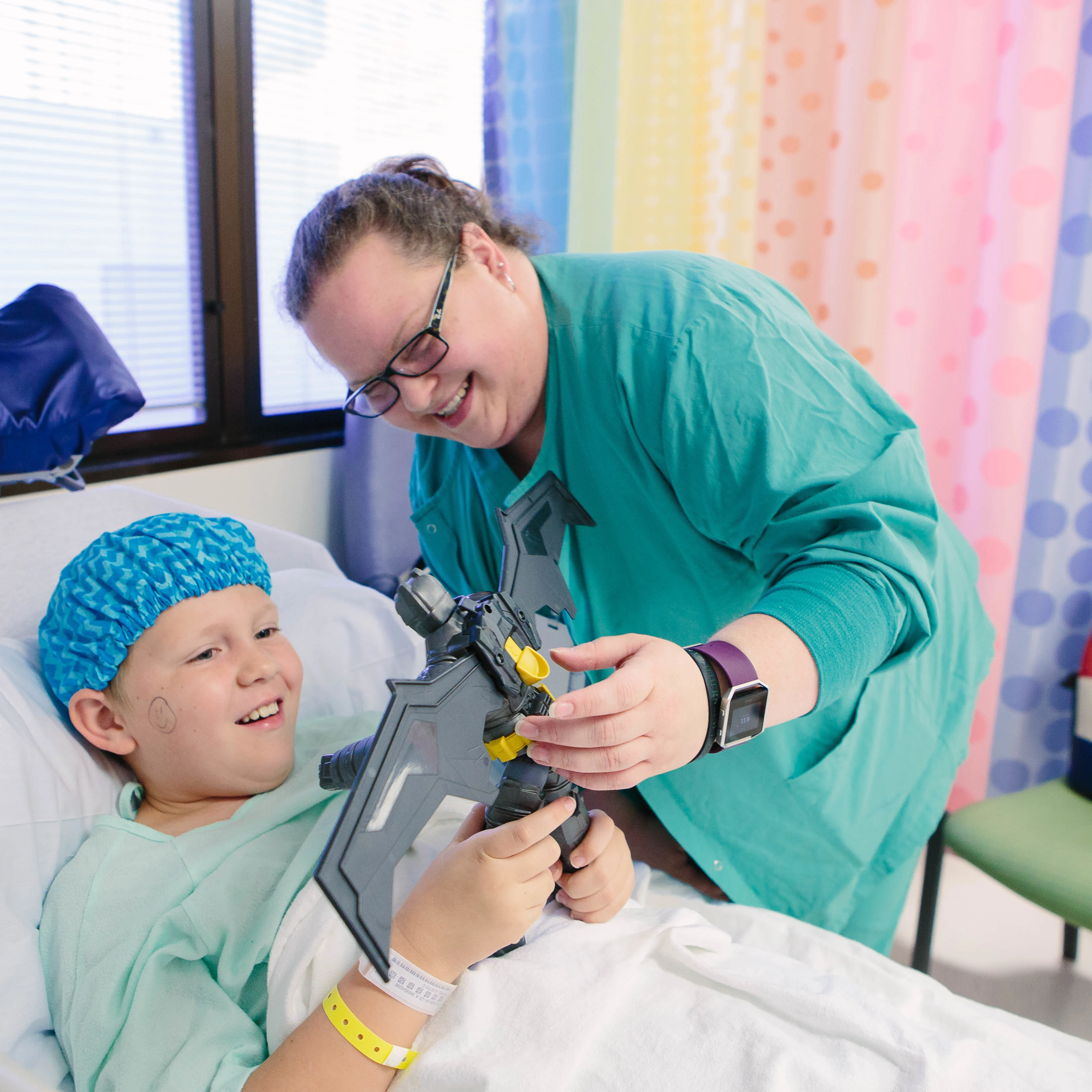 Wolfson medical professional plays with a toy with a little boy in a hospital bed and hospital gown and cap