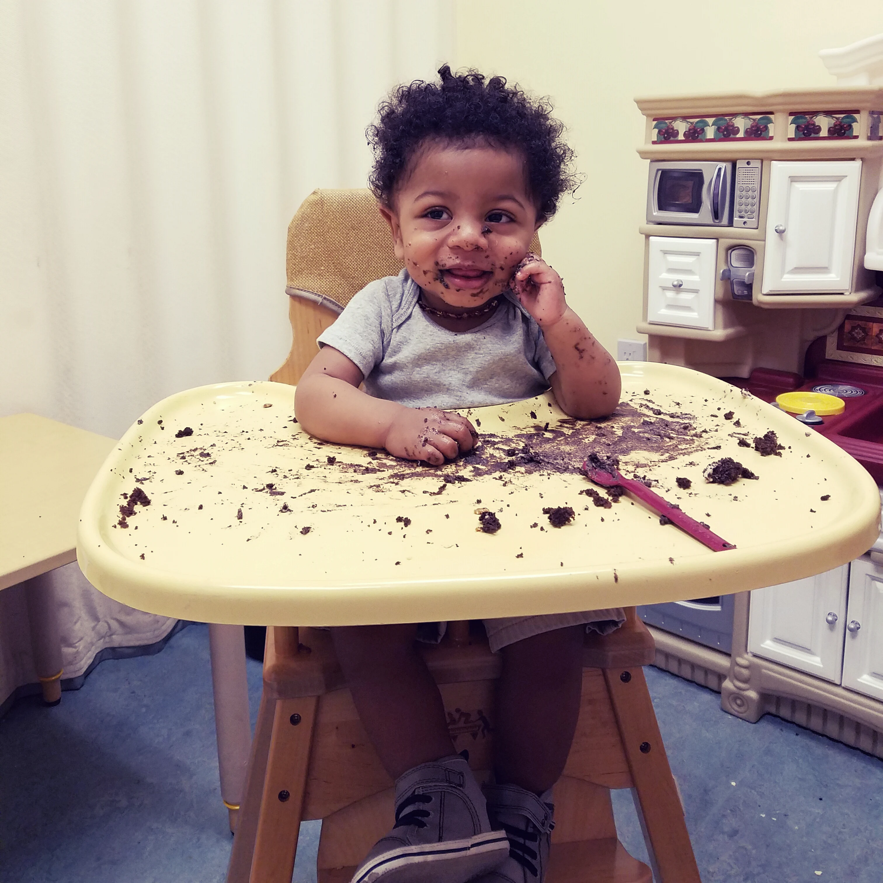 toddler boy sitting in a high chair smiling with chocolate cake all over the plate and his face.