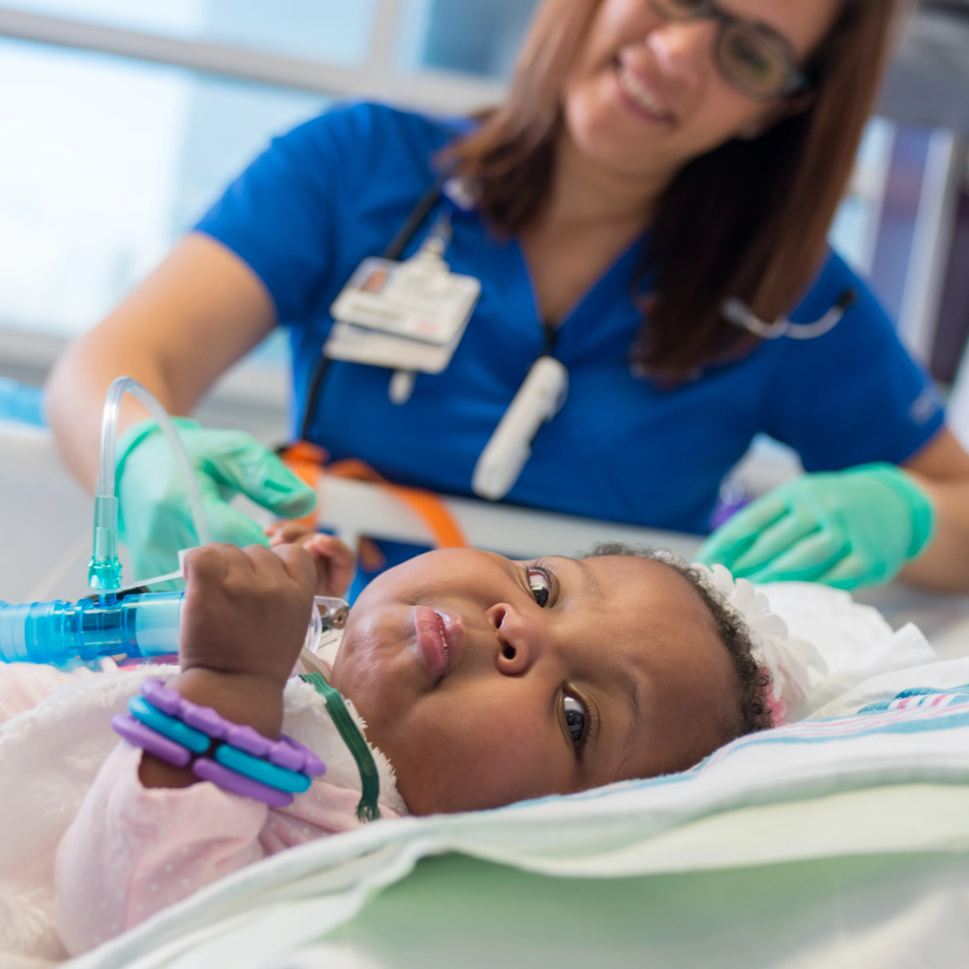 nurse holding the hand of a baby in the PICU