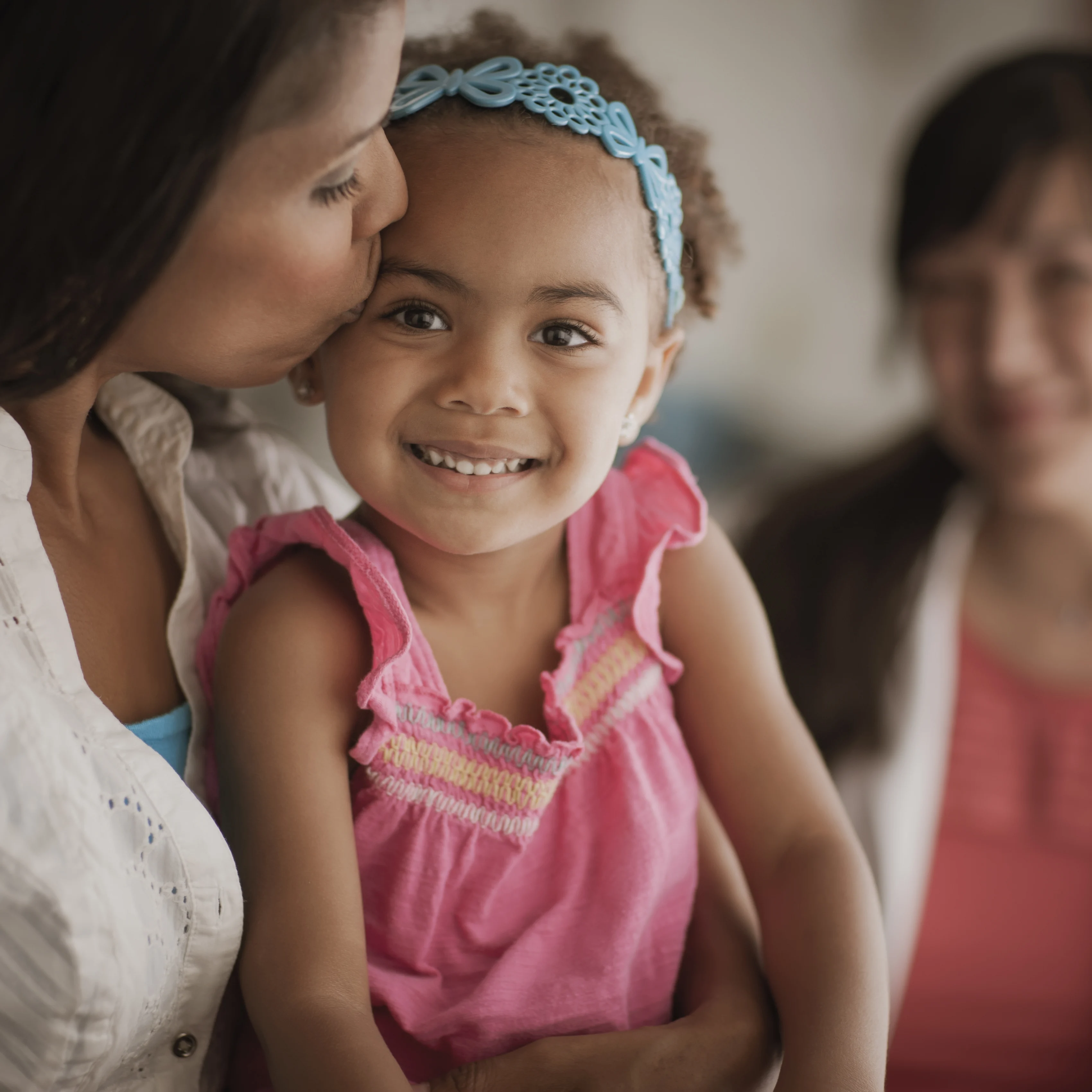 mom kissing smiling daughter on forehead while doctor looks on
