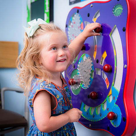 small smiling girl playing with a puzzle on the wall in a hospital room