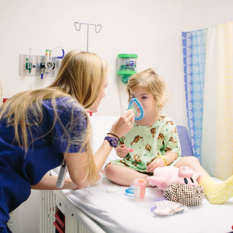 child life specialist fits young girl in hospital bed with a face mask