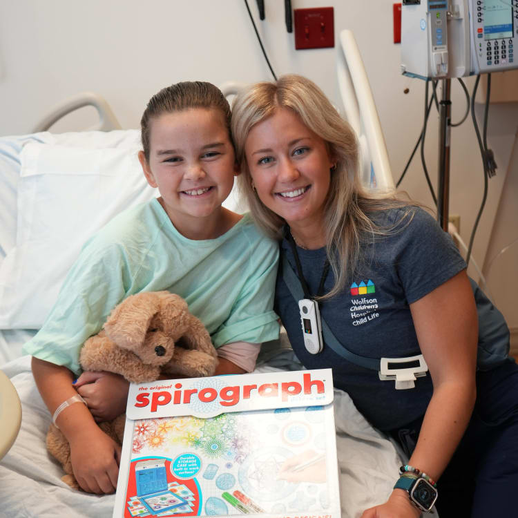 child life specialist next to a smiling pediatric patient in her hospital bed