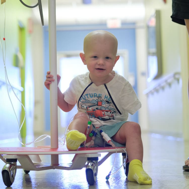 little boy who is a Wolfson patent sitting on an IV card in a lit hallway of the hospital.