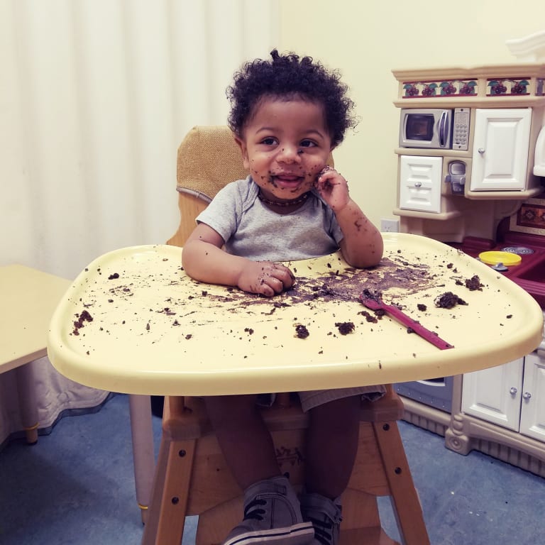 toddler boy sitting in a high chair smiling with chocolate cake all over the plate and his face.