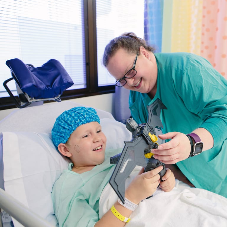 Wolfson medical professional plays with a toy with a little boy in a hospital bed and hospital gown and cap