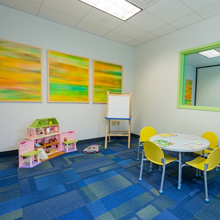 a room that has a kids table with puzzles, a dollhouse and an easel
