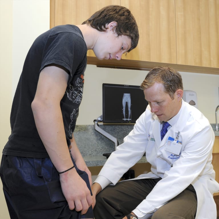 male doctor examining the knee of a teenage boy in a medical office